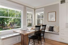 a dining room table with four chairs and a bench in front of two windows that look out onto the yard