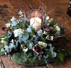 a candle that is sitting on a table with flowers and greenery in front of it