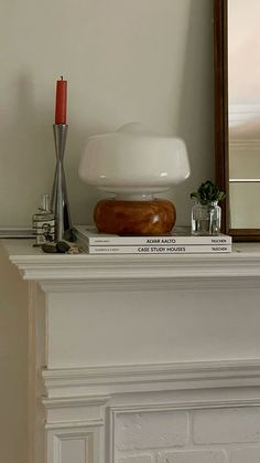 a white fireplace mantel topped with books and a candle next to a mirror on top of it