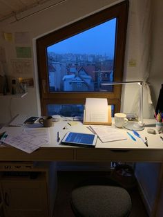 a desk with a laptop and papers on it in front of a window overlooking the city