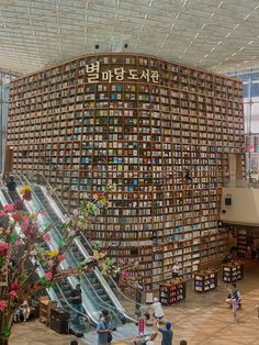 people are walking around in front of a huge bookcase with an escalator