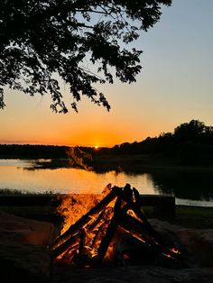 the sun is setting behind a campfire with water in the background and trees to the side