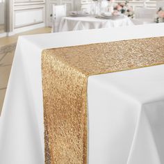 a gold table runner is on top of a white table with flowers in the background