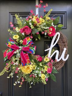 a wreath with the word h u on it and flowers hanging from it's front door