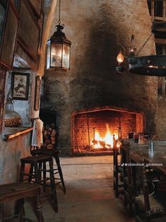 a fireplace in a stone walled room with wooden tables and stools next to it