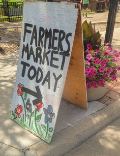 a sign that says farmers market today next to some potted flowers on the sidewalk