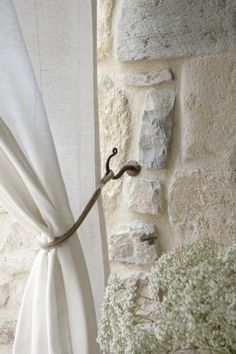 a white curtain hanging on the side of a stone wall next to a potted plant