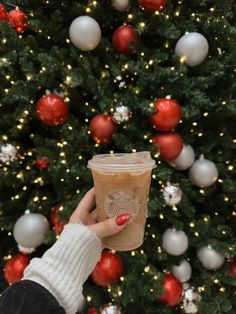 a person holding up a cup in front of a christmas tree with ornaments on it