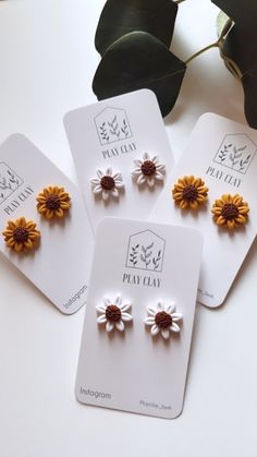 three pairs of flower studs sitting on top of a white table next to a plant