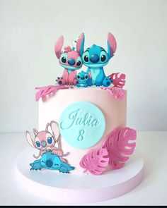 a pink and blue cake with two little stitchers on it's top, sitting on a white plate