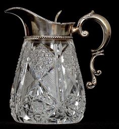 an old fashioned glass pitcher with a silver handle on a black background, the pitcher is empty