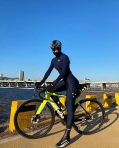 a woman in a wetsuit riding a bike on the road next to some water