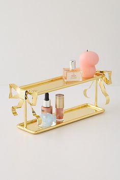 a gold shelf with cosmetics and perfumes on it in front of a white wall