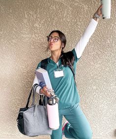 a woman with glasses holding up a cell phone and a book in her hand while standing next to a wall