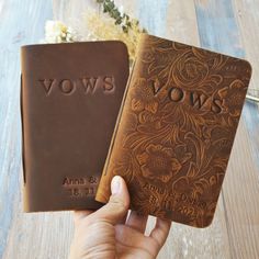 two brown leather books with the word vows written on them, held in someone's hand