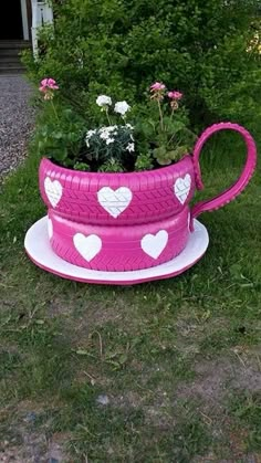 a pink coffee cup planter with hearts on it sitting in the grass next to flowers