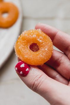 a hand holding an orange donut with white dots on it and a red polka dot nail polish