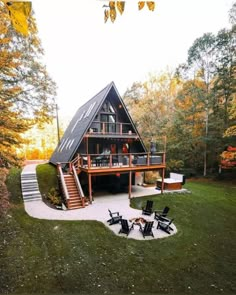 a large house in the middle of some trees with lawn chairs and fire pit around it