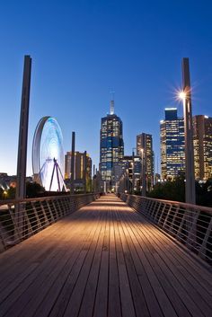 a wooden walkway leading to a ferris wheel in the middle of a city at night