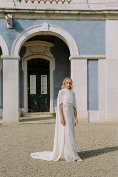 a woman standing in front of a building wearing a white dress with cape on it