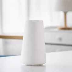 a white vase sitting on top of a table next to a lamp in a room