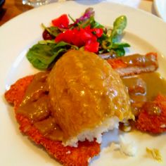 a white plate topped with meat covered in gravy next to vegetables and sauce