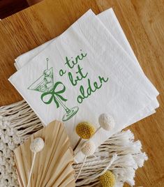 two napkins with green lettering on them sitting next to a fan and other items