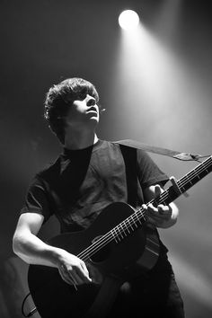 a man holding a guitar while standing in front of a spotlight filled stage with his eyes closed