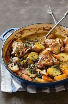 a blue pot filled with meat and potatoes on top of a white towel next to a fork