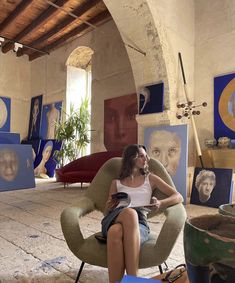 a woman sitting in a chair with paintings on the wall