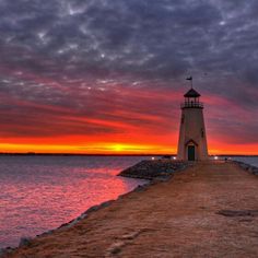 a light house sitting on top of a pier next to the ocean under a cloudy sky