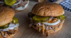 three hamburgers with pickles and cheese on them sitting on a wooden cutting board