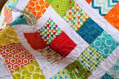 a multicolored quilt is displayed on a table top with an orange, green, blue, and white pattern