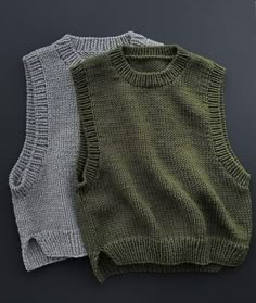 two sweaters sitting next to each other on top of a black surface, one in grey and the other in green