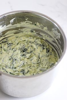 a metal bowl filled with green sauce on top of a white counter