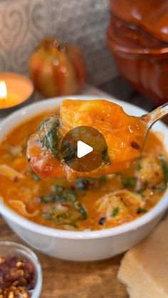 a spoon full of soup being lifted from a bowl with bread and other food items around it