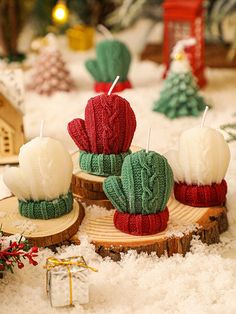 three knitted cactus candles sitting on top of snow covered ground next to small christmas trees