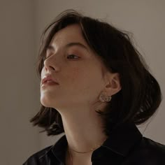 a woman with short hair wearing a black shirt and silver earrings looking off into the distance