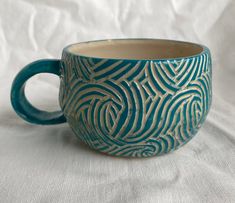 a blue and white coffee cup sitting on top of a white cloth covered tablecloth