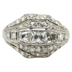 This platinum diamond ring is on the cusp of the Edwardian and Art Deco eras. The centerpiece of the ornate ring are three Peruzzi cut bezel set diamonds—one is an elongated rectangular shape, while the diamonds on either side are truncated, cut specifically for this ring. The larger diamonds are surrounded by a selection of 40 single and Old Mine Cut diamonds that are bead set into the ring. The ring has layers divided by milgrain work that tie together the lace-like patterns of the Edwardian e Persian Turquoise Ring, Antique Cocktail Ring, Platinum Diamond Ring, Ornate Ring, The Ring Face, Edwardian Ring, Platinum Diamond Rings, Square Stone, Gold Cocktail Ring