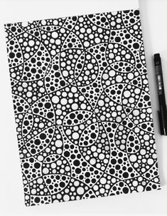 a black and white dotted notebook next to a pen