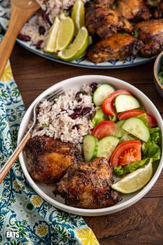 two plates with chicken, rice and vegetables on them next to a bowl of salad