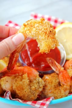 a person dipping sauce on some shrimp in a bowl with lemon wedges and ketchup