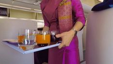 a woman holding a tray full of oranges and juice in her hand while standing on an airplane