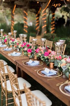 a long wooden table topped with lots of plates and place settings covered in pink flowers