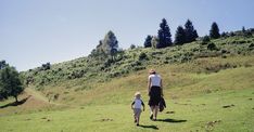 a man and child are walking in the grass on a hill with trees behind them