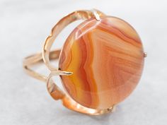 This elegant ring is designed with a stunning round cut agate. This eye-catching piece adds a touch of sophistication to any outfit. Made with yellow gold, this cocktail ring is sure to make a statement and elevate your style!Metal: 14K Yellow GoldGem: Agate 8.56 CaratsGem Measurements: 18.1 mm, RoundRing Size: 5.25Marks: "14K" Stamped on the inside band Yellow Gold Cocktail Ring, Right Hand Ring, Gold Cocktail Ring, Gold Cocktail, Right Hand Rings, Hand Ring, Cabochon Ring, Agate Jewelry, Banded Agate