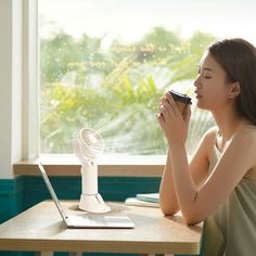 a woman sitting at a table drinking from a cup