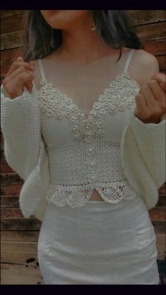 a woman wearing a white top and skirt with lace detailing on the bottom, standing in front of a wooden wall