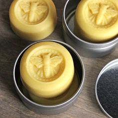 four tins filled with yellow wax sitting on top of a wooden table next to each other